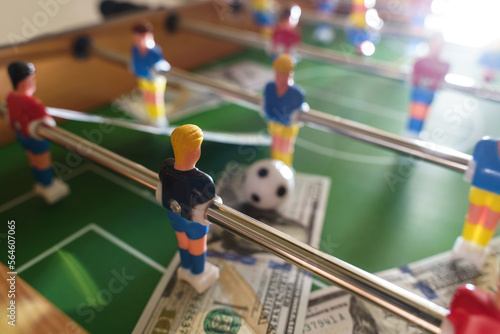 Schilderij op canvas Table football game with US dollar bills scattered around it, alluding to a bett
