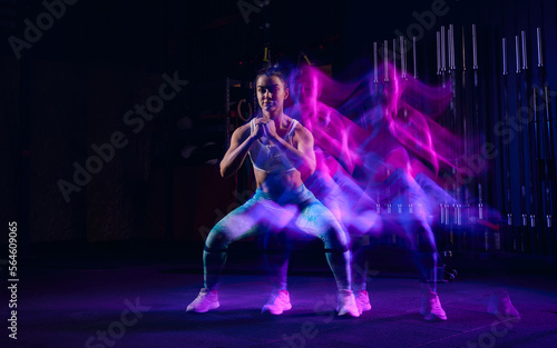Workout at gym. Sportive woman in sportswear and sportsfoot training in modern fitness room over dark background with mixed neon light. Active and healthy lifestyle