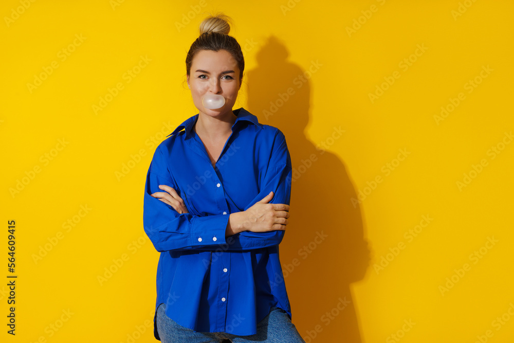 Happy woman blowing a bubble with chewing gum against yellow background Happy woman blowing a bubble with chewing gum against yellow background