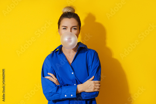 Happy woman blowing a bubble with chewing gum against yellow background © blackday