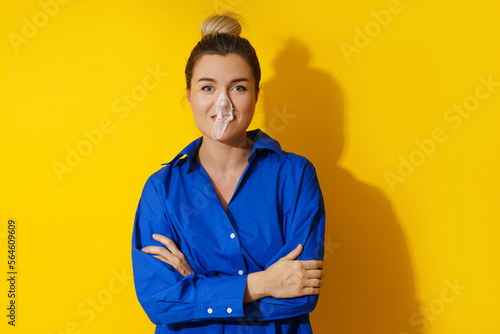 Happy woman blowing a bubble with chewing gum against yellow background