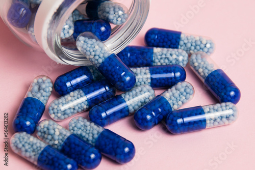 Vitamins in tablet form. Blue pills and transparent jar close-up on pink paper background