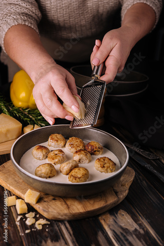 woman grating parmesan on meatballs in cream sauce