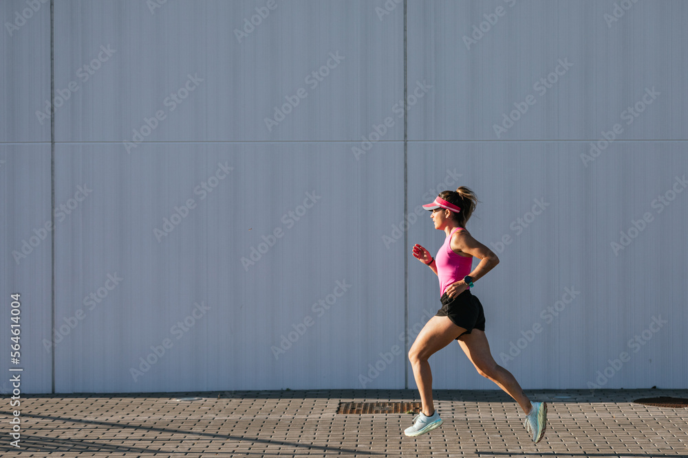 Sporty woman running in the street. Pink clothes and cap. Health concept. Sporty woman running in the street. Pink clothes and cap. Health concept.