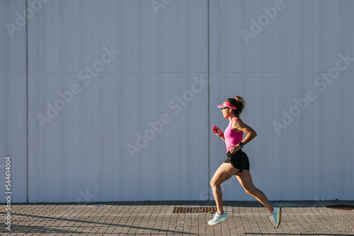 Sporty woman running in the street. Pink clothes and cap. Health concept.