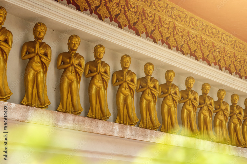 Row of golden Buddha statues, each in a praying posture, situated in an ancient Thai temple