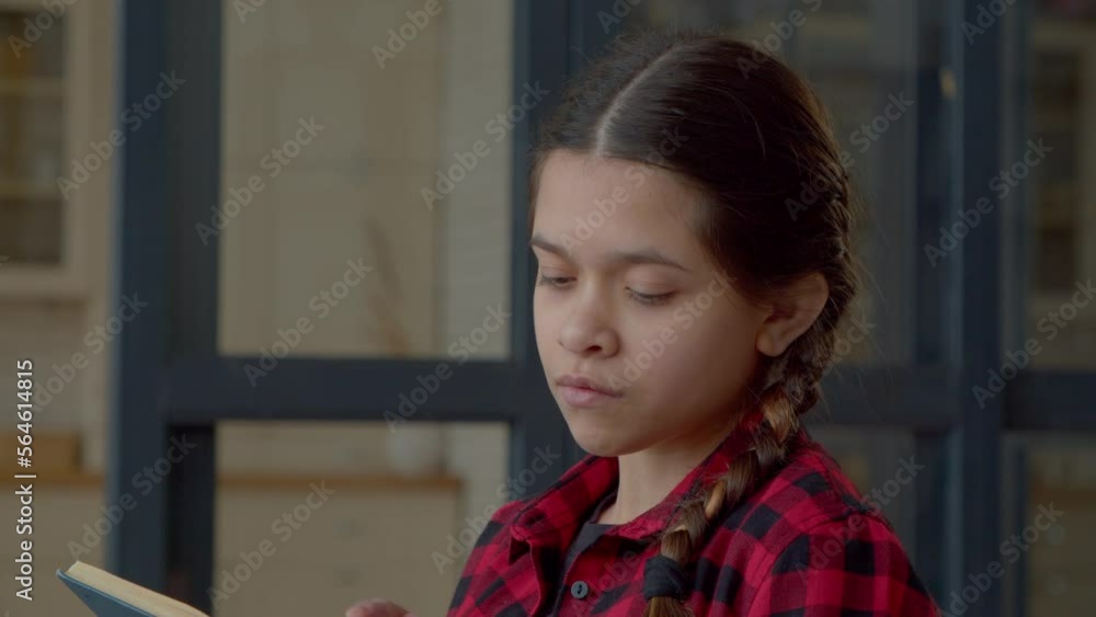 Portrait of thoughtful engrossed in reading attractive Latin teen girl with active imagination and stylish pigtails spending pastime, enjoying imaginative literature while relaxing indoors. Portrait of thoughtful engrossed in reading attractive Latin teen girl with active imagination and stylish pigtails spending pastime, enjoying imaginative literature while relaxing indoors.