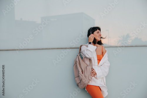 European dark-haired care woman holding backpack listening music in headphones at the street. Staying with copy space for your advertising. Lifestyle concept 