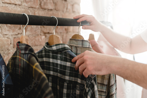 Man is browsing through various shirts hanging on the clothing rack in the wardrobe © blackday