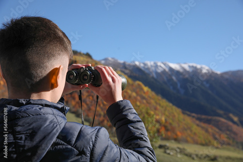 Boy looking through binoculars in mountains on sunny day. Space for text