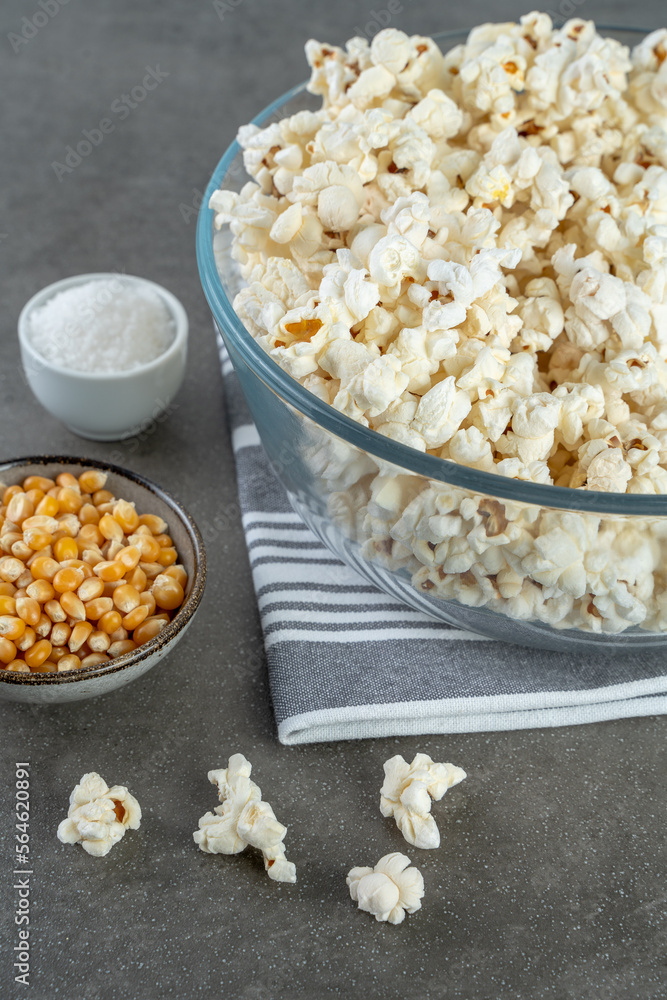 popcorn in a bowl, salt and popcorn kernels on a gray striped napkin on a gray concrete background, close-up and selected focus. popcorn in a bowl, salt and popcorn kernels on a gray striped napkin on a gray concrete background, close-up and selected focus.