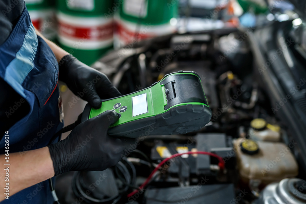 Male auto mechanic with an electronic device for checking a car in a car service garage. Car maintenance and repair Male auto mechanic with an electronic device for checking a car in a car service garage. Car maintenance and repair