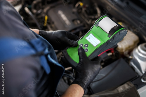 Male auto mechanic with an electronic device for checking a car in a car service garage. Car maintenance and repair