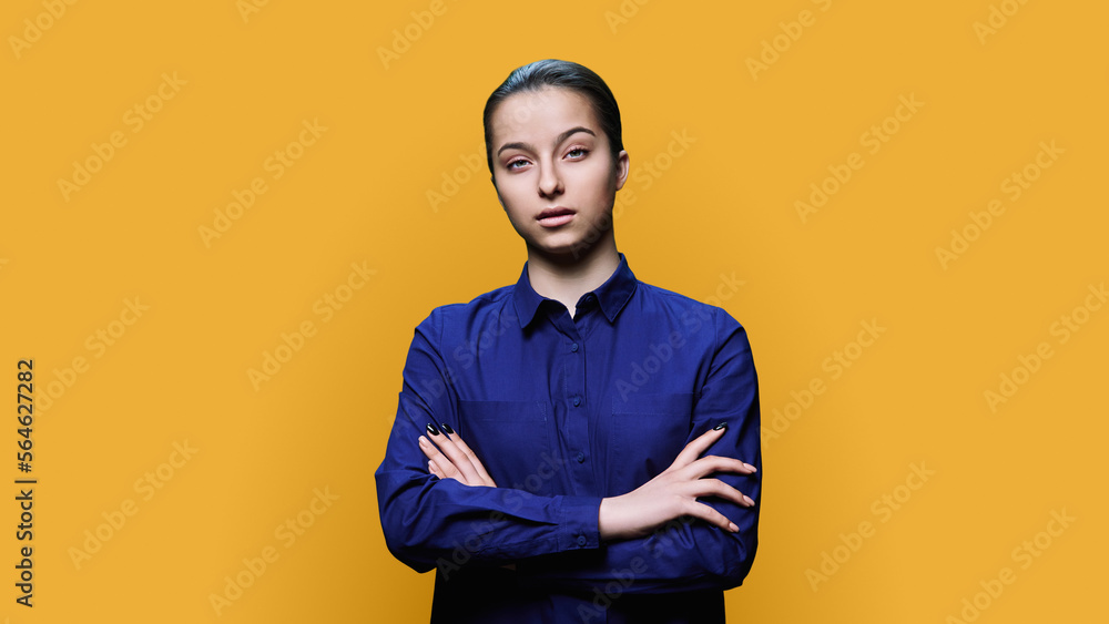 Obraz premium Young serious female with crossed arms on yellow background