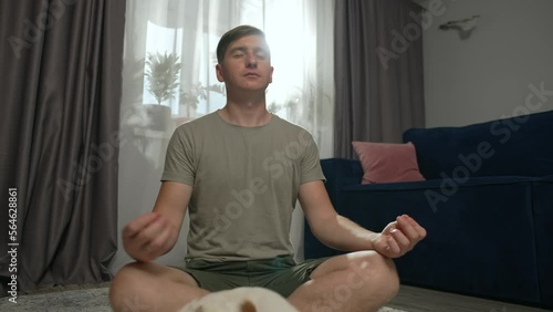A man practices yoga at home, sits in the lotus position next to his dog. The dog interferes with doing yoga in the room. Yogi in the living room. High quality 4k footage