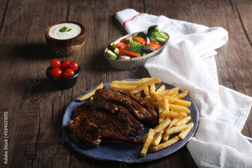 Grilled steak with french fries served with vegetables, cherry tomatoes, and garlic sauce on a plate on a wooden table