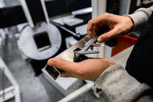 Close up of mans hands inspecting laser cut of metal square tube with vernier caliper.