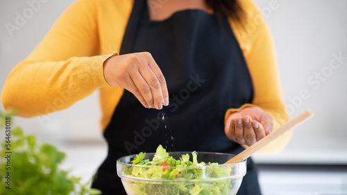 Fotografie Millennial african american woman in apron salting salad, cooking dinner at tabl