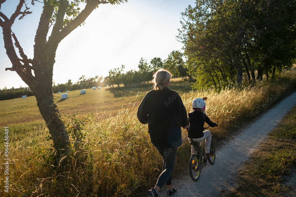Mother teaching kid to ride bicycle on dirt road Mother teaching kid to ride bicycle on dirt road
