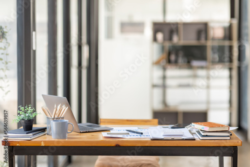 Laptop Computer, notebook, and eyeglasses sitting on a desk in a large open plan office space after working hours	 photo