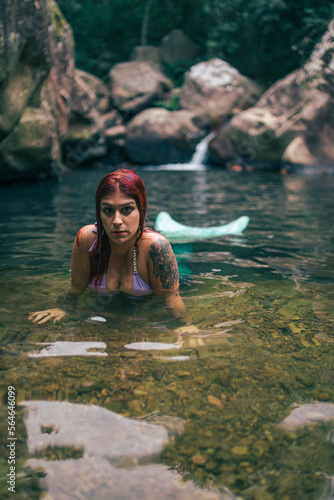Fototapeta Naklejka Na Ścianę i Meble -  Sirena pelirroja en una gruta rio con agua encantado manantial misterioso en bosque frondoso y verde