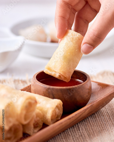 Grabbing an egg roll with his hands and dipping it in red sauce at