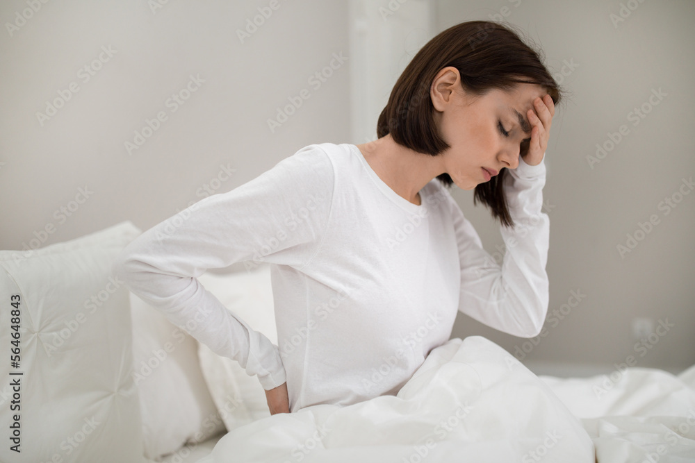 Tired woman suffering from back pain at home in bedroom Tired woman suffering from back pain at home in bedroom