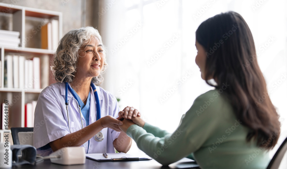 Woman senior doctor is Reading Medical History of Female Patient and Speaking with Her During Consultation in a Health Clinic. Physician in Lab Coat Sitting Behind a Laptop in Hospital Office. Woman senior doctor is Reading Medical History of Female Patient and Speaking with Her During Consultation in a Health Clinic. Physician in Lab Coat Sitting Behind a Laptop in Hospital Office.