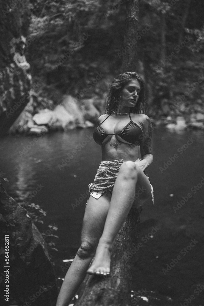 Fototapeta premium Chica guapa morena española en bikini en un rio de un bosque verde frondoso y natural
