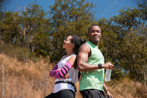 Athlete couple standing drink water while running in the forest during vacation. African American man and woman runner sport training together. Colleague workouts running and healthy lifestyle.