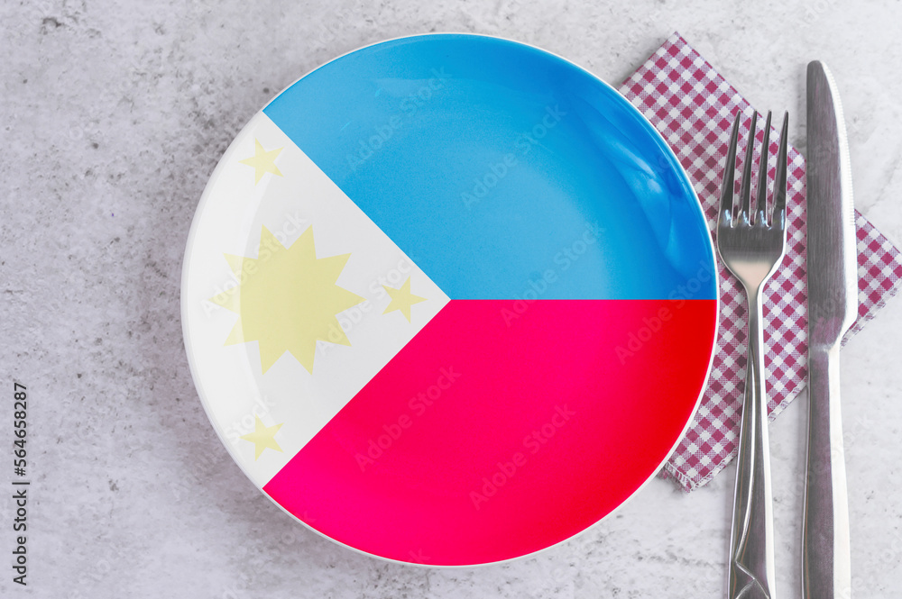 Naklejka premium A Plate with the Flag of Philippines, Cutlery and Napkins on the Mable Table.