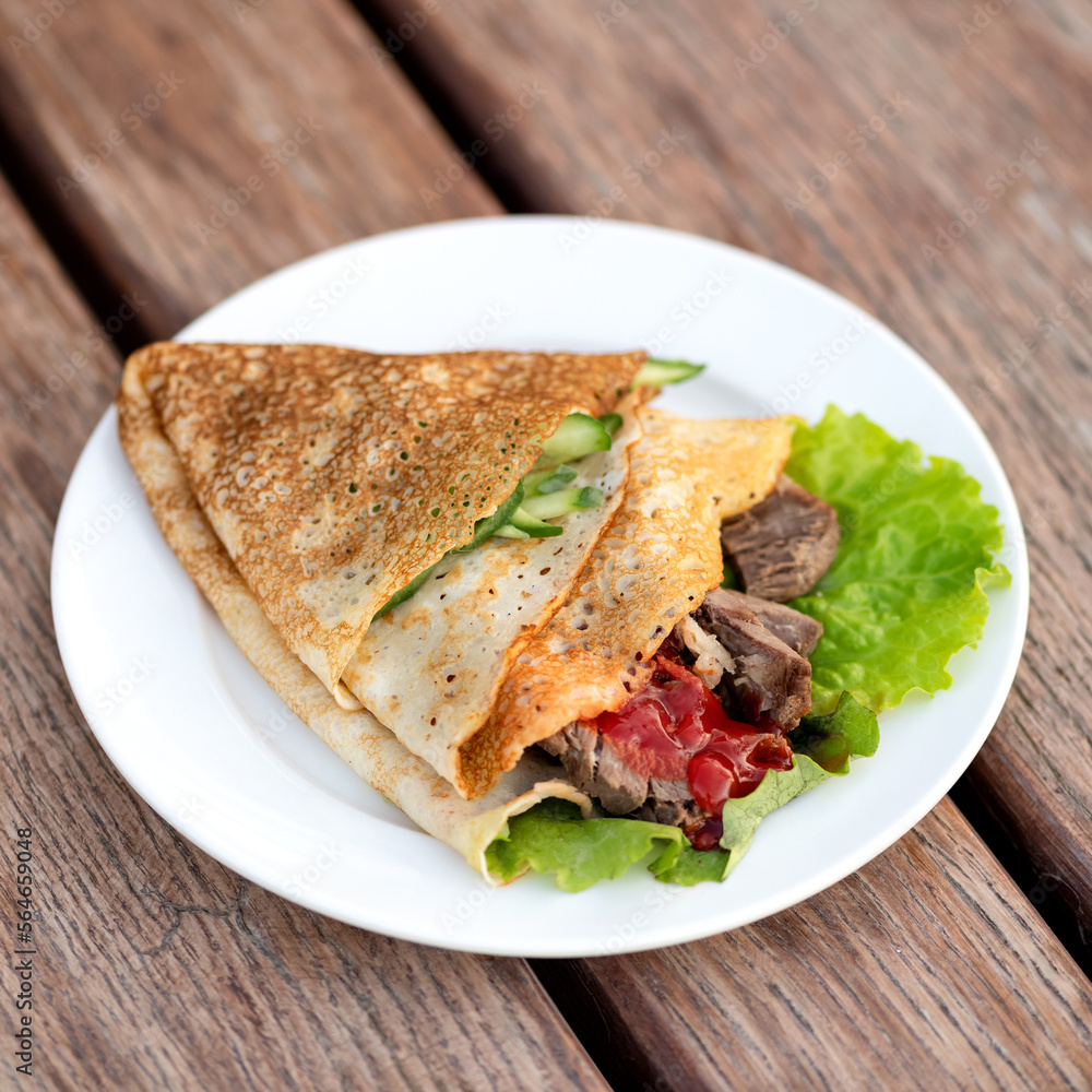 Spring roll for breakfast in restaurant. Pancake with salad, vegetables and meat wrapped in corner. Dish in plate on wooden table. View from above. Soft focus. Copy space. Wooden background. Spring roll for breakfast in restaurant. Pancake with salad, vegetables and meat wrapped in corner. Dish in plate on wooden table. View from above. Soft focus. Copy space. Wooden background.