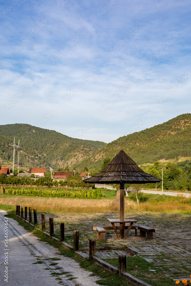 Small outdoors rural rest place with wooden umbrella, benches and a table. Beautiful green hills of a mountain in the background. Western Serbia, Balkans