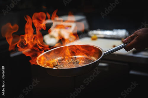 Chef hand in restaurant kitchen with pan, cooking flambe on shrimps