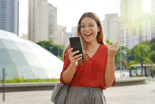Fotografia Brazilian surprised girl watching joyful her smartphone with modern sustainable