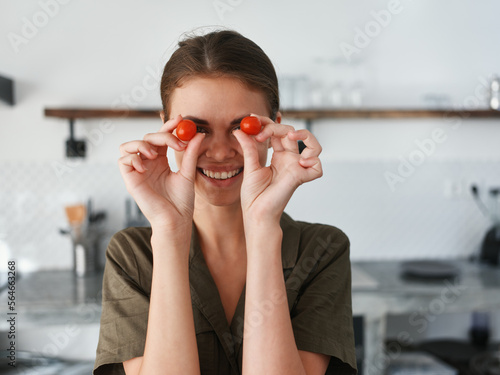 A woman at home in the kitchen prepares food and has fun taking tomatoes in her hands and putting them on her eyes, lifestyle