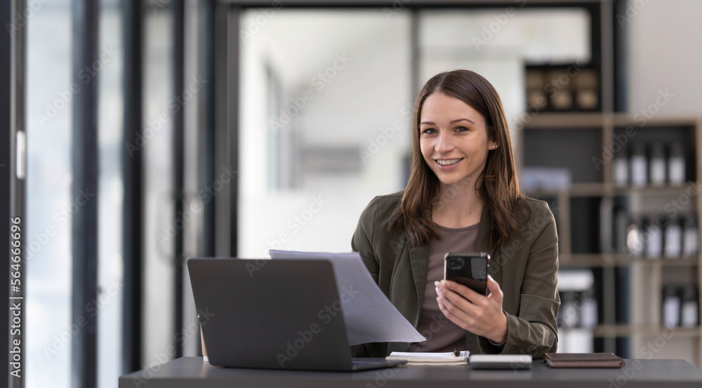 Smiling beautiful Asian businesswoman analyzing chart and graph showing changes on the market and holding smartphone at office. Smiling beautiful Asian businesswoman analyzing chart and graph showing changes on the market and holding smartphone at office.