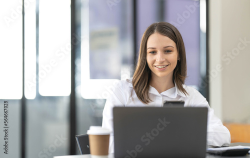Smiling beautiful Asian businesswoman analyzing chart and graph showing changes on the market and holding smartphone at office.
