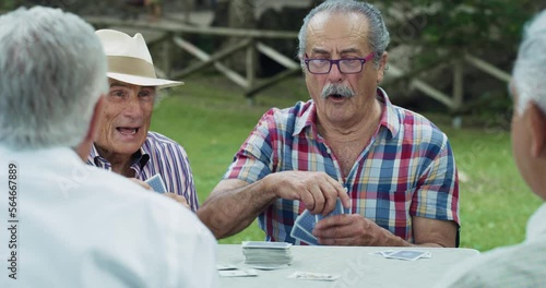 Portrait of a Group of Senior Male Friends Enjoying the Summer Weather Outdoors by Playing Cards Game Together in a Park. Old Player Getting Lucky with the Winning Card, Ending the Game with Victory  photo