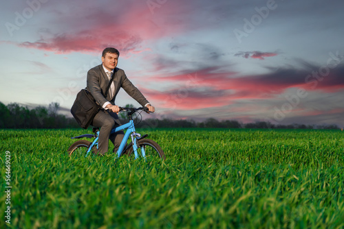 a businessman rides a bicycle with a briefcase on a green grassy field, dressed in a business suit, beautiful nature in spring, freelance business concept