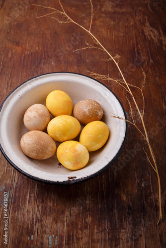 Yellow and brown Easter eggs in white bowl on wooden table. Spring holiday, happy easter concept. Vertical shot