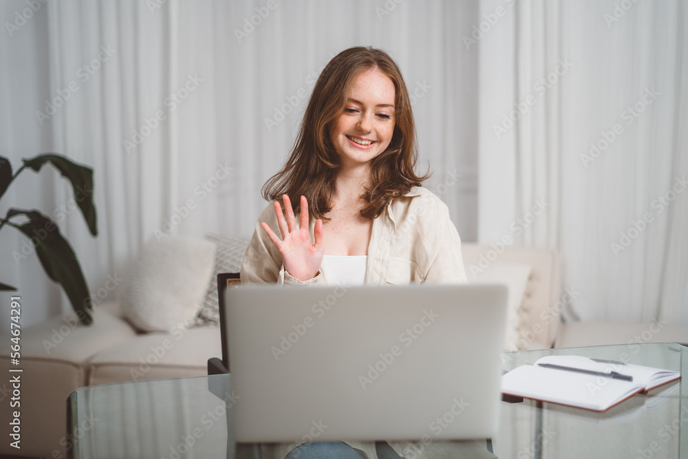 Happy young business woman employee, hr manager having remote online work hybrid meeting or distance job interview waving hand looking at laptop during virtual video conference call in office Happy young business woman employee, hr manager having remote online work hybrid meeting or distance job interview waving hand looking at laptop during virtual video conference call in office