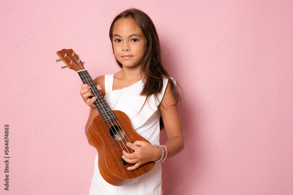 Cute little girl in summer clothing playing ukulele over pink background. Happy vacation concept. Cute little girl in summer clothing playing ukulele over pink background. Happy vacation concept.