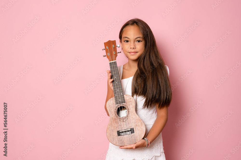 Cute little girl in summer clothing playing ukulele over pink