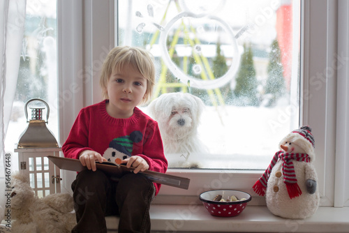 Cute blond toddler child, sitting on the window, looking at the snow falling outside photo