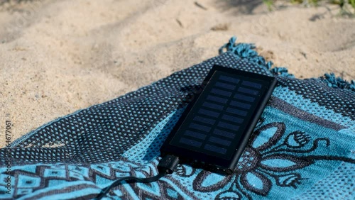 Solar panel charging a mobile phone on a beach. Portable powerbank solar charger in sunlight. Sun energy.