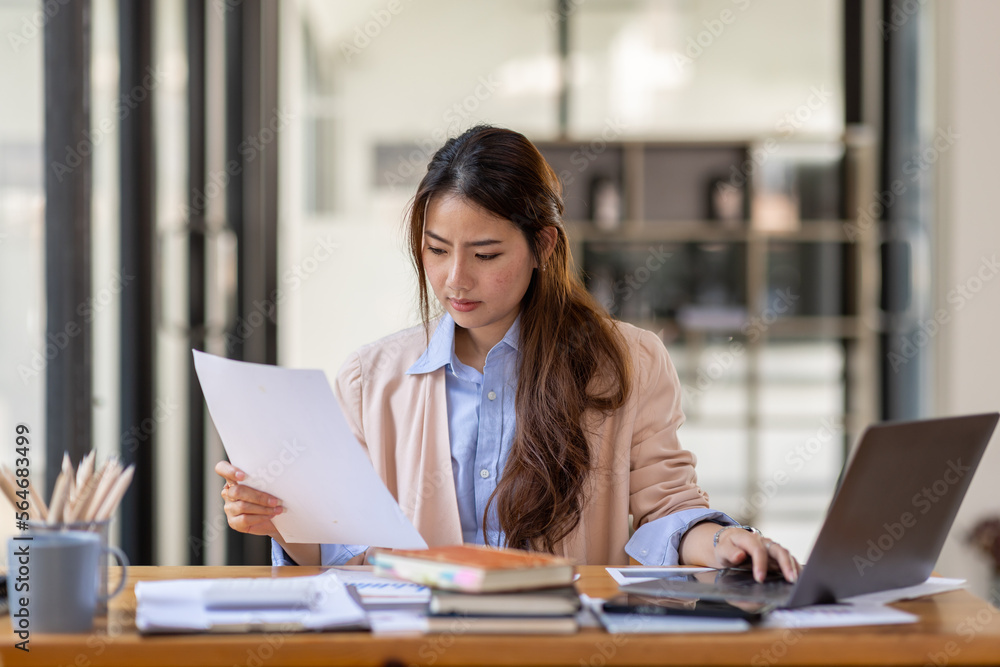 Thai Asian businesswoman working inside office with documents and laptop, worker paperwork calculates financial indicators smiling and happy with success and results of achievement and work Thai Asian businesswoman working inside office with documents and laptop, worker paperwork calculates financial indicators smiling and happy with success and results of achievement and work
