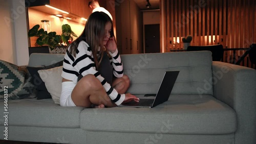 The girl is setting on the couch and working from home, the guy is cooking in the background. The concept of remote work