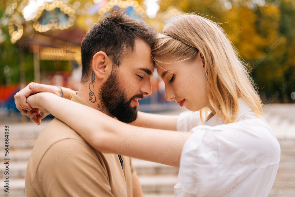 Close up of romantic young couple in love touching each other foreheads hugging standing with closed eyes in park in summer day. Handsome bearded man and blonde woman enjoying weekend outdoors. Close up of romantic young couple in love touching each other foreheads hugging standing with closed eyes in park in summer day. Handsome bearded man and blonde woman enjoying weekend outdoors.