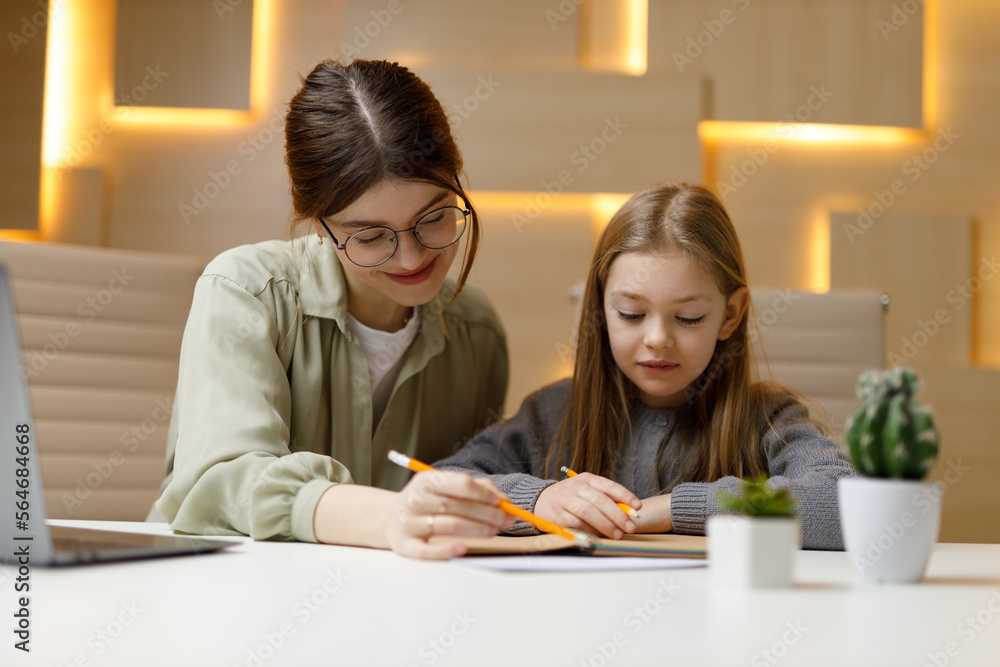Teacher and student at the desk, mother helps her daughter do homework, private children's tutor.